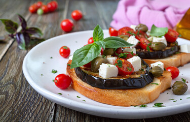 Garlic bruschetta with eggplant, feta, cherry tomatoes, capers. Useful vegetarian appetizer. Italian Cuisine.