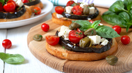 Garlic bruschetta with eggplant, feta, cherry tomatoes, capers. Useful vegetarian appetizer. Italian Cuisine.