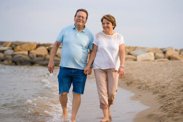 happy retired mature couple walking on the beach - pensioner woman and her husband taking romantic walk together enjoying sweet holidays in lifetime relationship and love