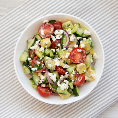 Delicious Avocado Tomato and Cucumber Salad in a bowl on cloth, overhead view. Flat lay, top view, from above.