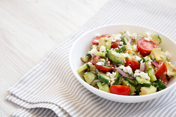 Tasty Avocado Tomato and Cucumber Salad in a bowl on a white wooden background, side view. Copy space.