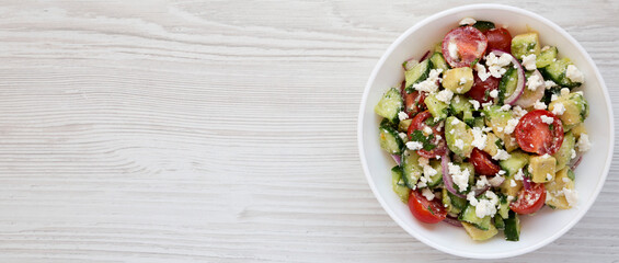 Tasty Avocado Tomato and Cucumber Salad in a bowl on a white wooden surface, top view. Space for text.