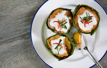 Steamed fish with curry paste in banana leaf cup and *Yor leaves (Thai herb)* in white dish  (Thai language called Hor mok) on old wooden table
