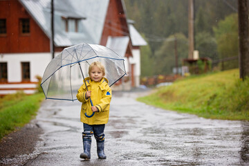 Cute blond toddler child, boy, playing in the rain with umbrella on a foggy autumn day