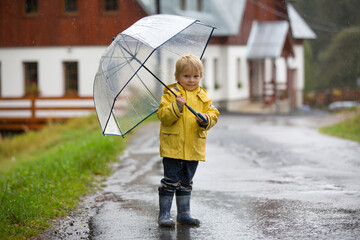 Cute blond toddler child, boy, playing in the rain with umbrella on a foggy autumn day