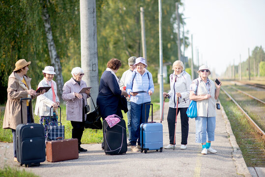 A group of positive senior elderly people travelers using tablets waiting for train before going on a trip