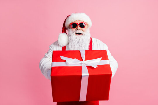 Portrait of his he nice attractive cheerful cheery Santa father holding in hands giving handling large giftbox congratulation congrats greetings North Pole isolated over pink pastel color background