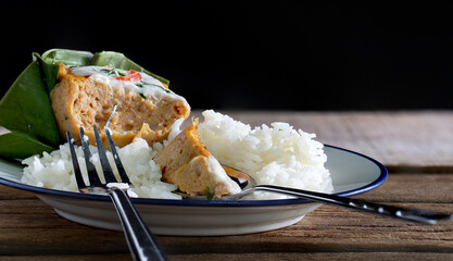 Cooked rice and Steamed fish with curry paste in banana leaf on old wooden table which has black background