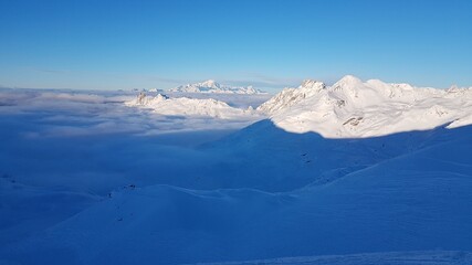 View of the snow-covered peaks of the French Alps, above a cloud cover with a sunny blue sky from the ski area Les Trois Vallees