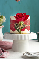 Vertical shot of a small fancy cake with a red rose on a white tray