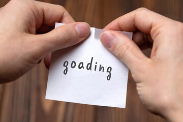 Hands of a man tearing a piece of paper with inscription goading