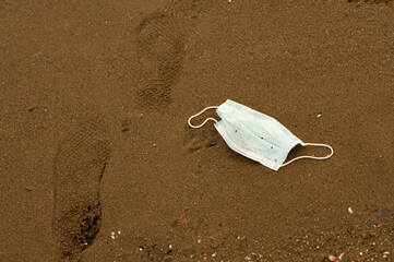 Waste during COVID-19 with footprints of man. Dumped into oceanic coronavirus single-use face masks. Environmental and coastal plastic pollution. Garbage on the beach