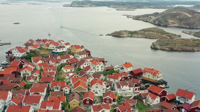 Island on Swedish west coast in drone shot. Densely populated land and granite rock islands with rooftop aerial over view. Homes and narrow buildings on Gullholmen Harmano in Orust Bohuslan Sweden