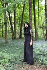 Spooky woman in long black dress walking through forest holding a single red rose