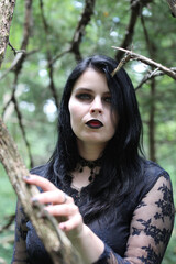 Naklejka premium Evil witch walking through thorn trees in the forest. Dark gothic makeup and long black dress.
