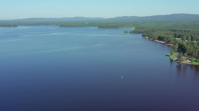 Swedish Scandinavian calm blue lake on beautiful summer morning with forest hills at camping ground site at shoreline. Single swimmer tiny dot on surface. Aerial drone shot in Sweden
