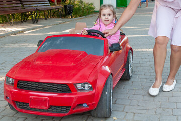 little beautiful girl rides in the park on a red electric machine on a summer day