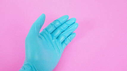 Close up of left hand wear latex glove on pink background.