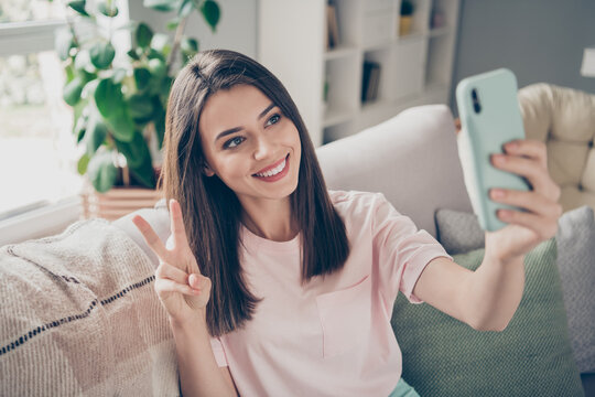 Photo of homey lady hold telephone make selfies show v-sign symbol sit sofa indoors