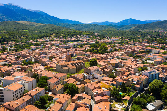 Aerial view of residential areas of Prades town with similar brownish roofs in green valley of French Pyrenees on summer day, Occitanie
