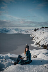 Fototapeta premium Lifestyle portrait of woman cuddled up in blanket posing in snow on an amazing sunny winter day in Scandinavia.