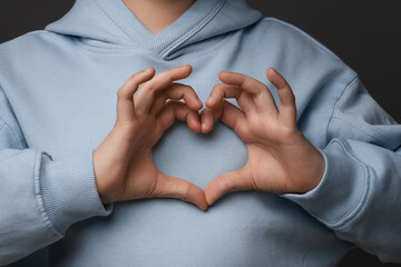 Cropped close up of boy making heart symbol by hands. Romantic concept. Studio shot, gray background
