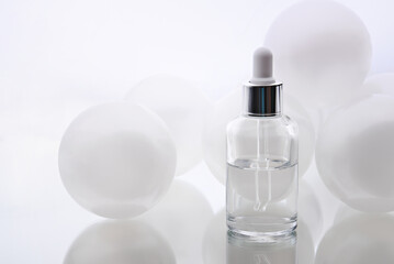Cosmetic serum. Eyedropper with a drop and a bottle on a white mirror surface.