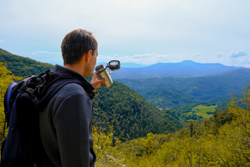 Man, hiker drinking beverage from a thermos in the mountains. Traveler with backpack. Equipment for trekking. Natural background. Copy space. High-quality photo
