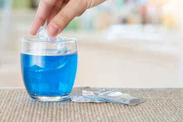 Close up on a female hand while plunges antibacterial effervescent tablets and orthodontic appliance in to a glass of water. Immersion of denture or bite inside a glass of water with disinfectant.