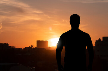 Silhouette of a man standing on top of building in front of city during sunset, concept picture