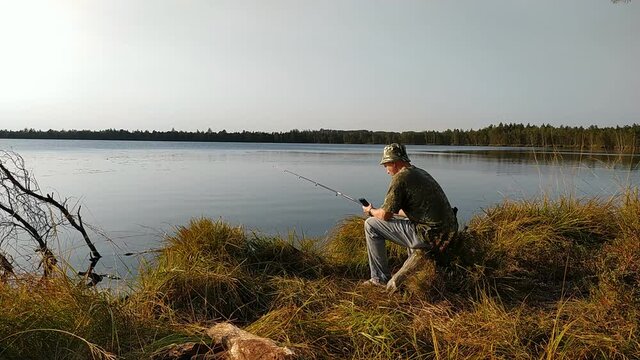 A fisherman in nature is fishing with a rod in the lake and reading the news on his phone