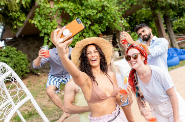 Group of young people having fun at summer vacation and enjoying a poolside party with drinks and making selfie.	