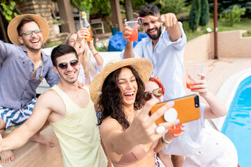 Group of young people having fun at summer vacation and enjoying a poolside party with drinks and making selfie.	