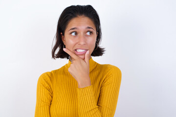 Young hispanic girl with short hair wearing casual yellow sweater isolated over white background Thinking worried about a question, concerned and nervous with hand on chin.