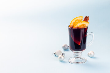 Red glogg or mulled wine with orange slices and cinnamon stick, Christmas toys on a blue background, horizontal, copy space