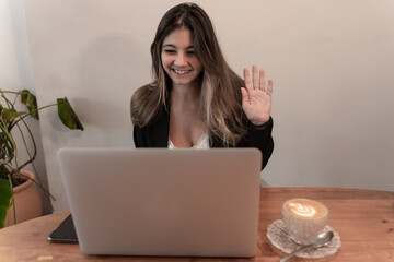 Pretty elegant businesswoman waving while smiling on video call or virtual meeting at breakfast and coffee time