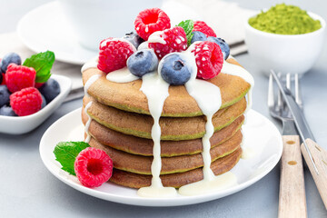 Matcha pancakes served with condensed milk, blueberry and raspberry on  white plate, horizontal
