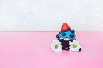 beautiful cupcake decorated with strawberries, blue cream and bright lights for the holiday on a pink background