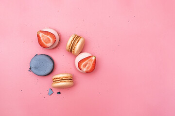 five round macaroni of different colors decorated with berries on a pink background