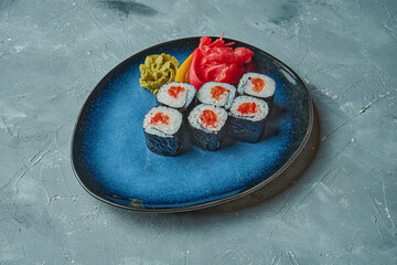 Sushi maki roll with salmon on a blue plate on a gray background. Japanese cuisine