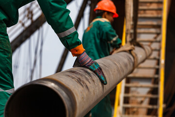 Two oil workers in green and orange work wear and suede gloves  with  rusted drilling pipe. Oil...