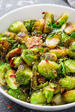 Close up on roasted / fried brussels sprouts in a white bowl with chili and garlic flakes seasoning. Fresh and cooked seasonal food.