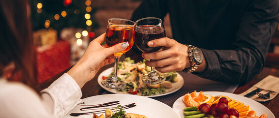 hands with glasses clinking against the background of Christmas tree lights and bonfires from a...