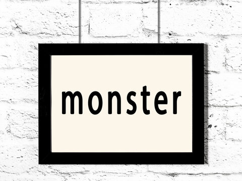 Black frame hanging on white brick wall with inscription monster