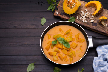 Curry or Pumpkin Soupserved in a black bowl placed on an old wooden floor, top view.