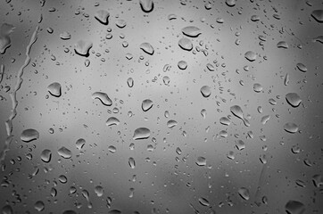 A dark photo of rain drops on a window. Raining on the glass black and white image with vignetting.