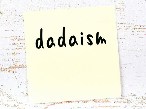 Yellow Sticky Note On Wooden Wall With Handwritten Word Dadaism