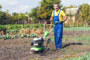 Man cultivates the ground in the garden with a tiller, preparing the soil for sowing