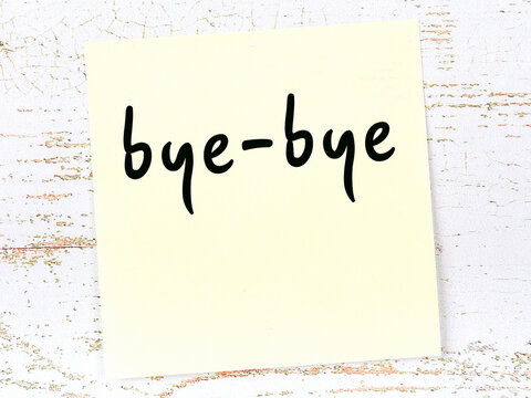 Yellow sticky note on wooden wall with handwritten word bye-bye