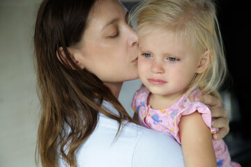 Young mother hugging her crying little daughter. Sad daughter in her mother's arms.	
